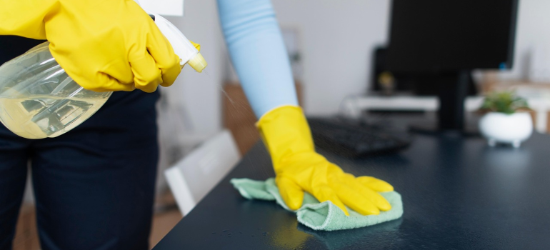 Osoba dezinfikuje sto pomoću sredstva za dezinfekciju i krpe.