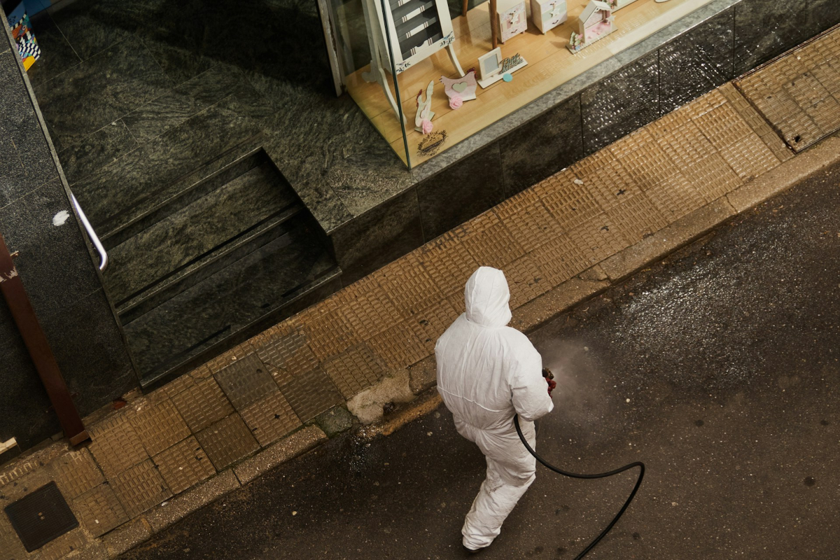 Radnik u zaštitnom odelu dezinfikuje trotoar ispred objekta